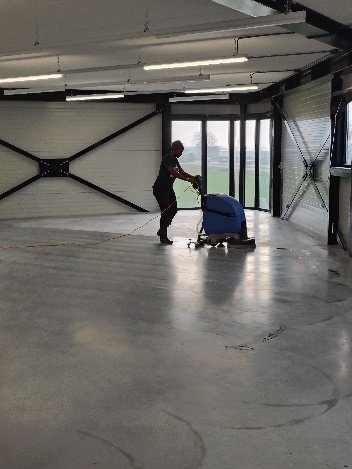 Medewerker van Maasstad schrobt een betonvloer in een bedrijfshal